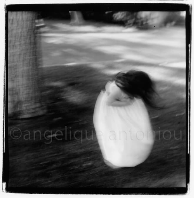 A child in a white dress spinning beneath a tree, blurred by the movement